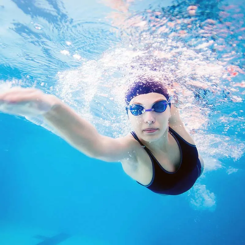 An adult swimmer in a cap and goggles mid-freestyle stroke, photographed from below the surface