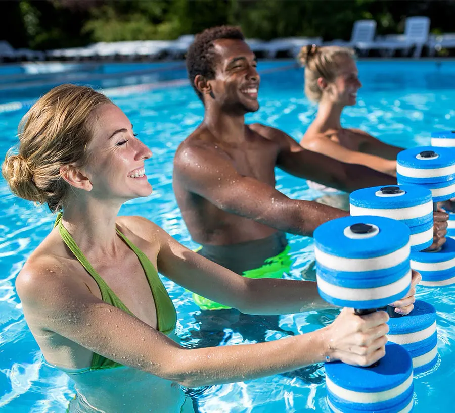 Three adults chest-deep in a pool, smiling, lifting blue and white foam dumbbells through the water