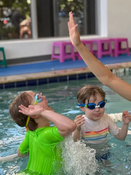 Two toddlers in the shallow end, laughing and splashing water at each other